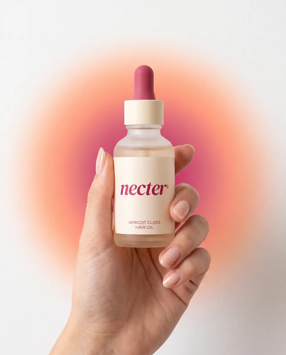 A hand holding the bottle up against a soft peach and raspberry glow