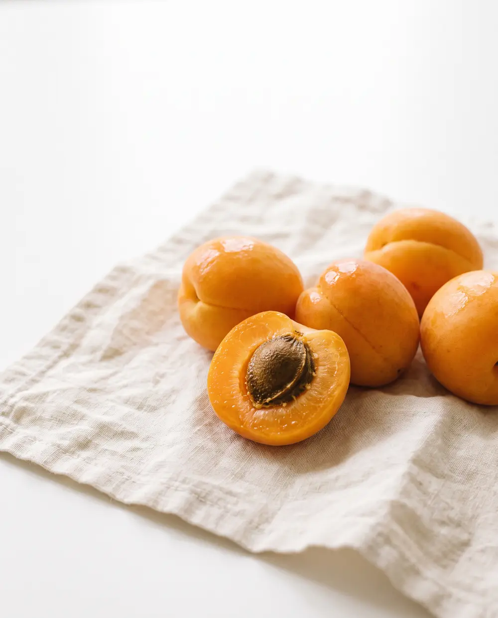 Ripe apricots on cream linen, one cut open to show its stone